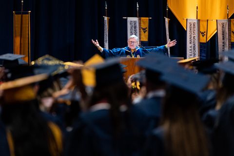 President Gee's face and outstretched arms are visible over a sea of mortarboards as he addresses graduates of the John Chambers College of Business and Economics.