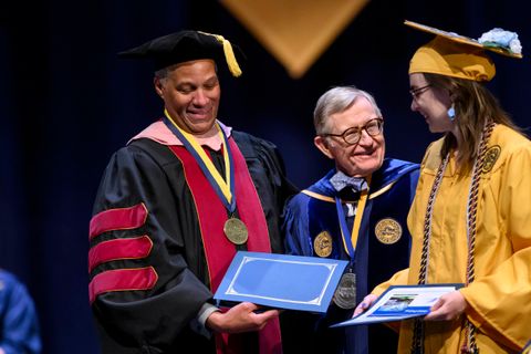 A graduate receives their diploma and is congratulated by Dean Keith Jackson and President Gordon Gee.