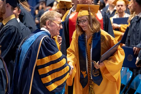 President Gee shakes hands with a Chambers College Honors graduate wearing a gold cap and gown.