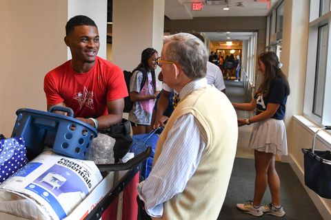 Student pushing a cart of belongings stops to talk with President Gee.
